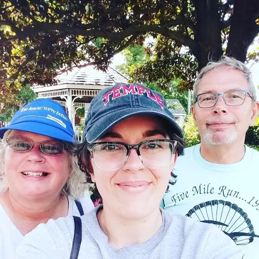 DeGeorge family subtly smiling in the shade under a tree in front of a white gazeebo