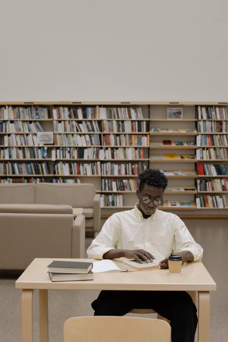 Black Man in White Dress Shirt Sitting on White Chair in the library