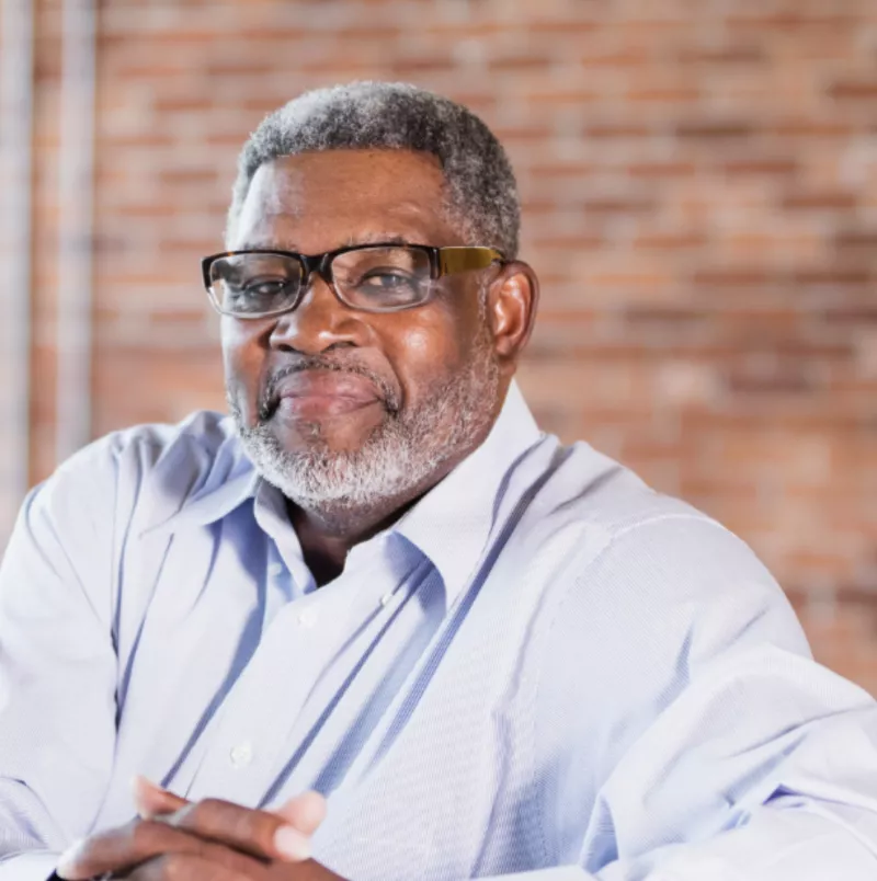 Black male smiling and posing for headshot wearing gold framed glasses
