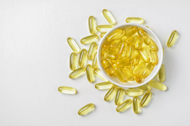 white bowl of yellow pill capsules overfilled onto white background