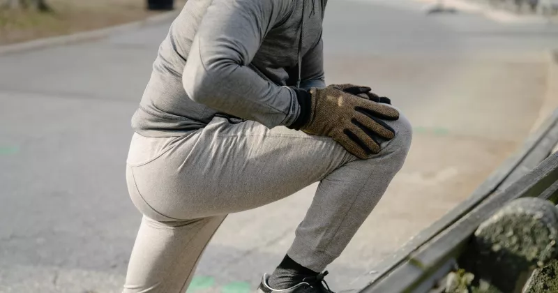 A man in cold weather jogging attire stretching on the side of the road