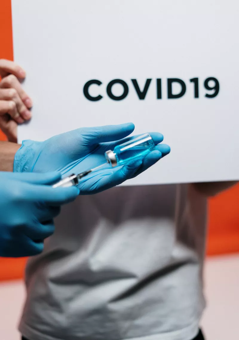 Person in gloves Holding Syringe in front of Covid19 sign