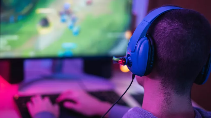 A man playing League of Legends on a colorful lit up back-lit desk wearing a blue headset