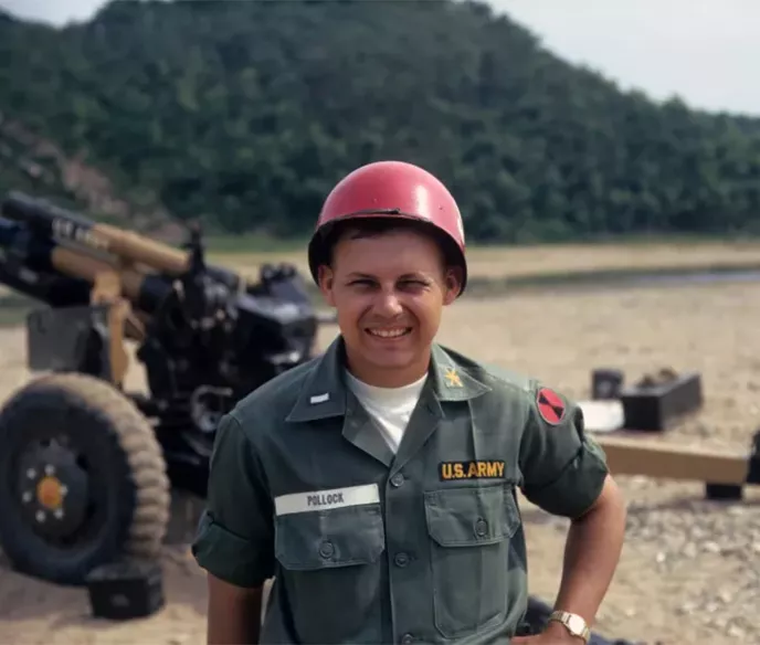 Us. Army man in uniform with red helmet standing in front of a M102 105mm towed wowitzer