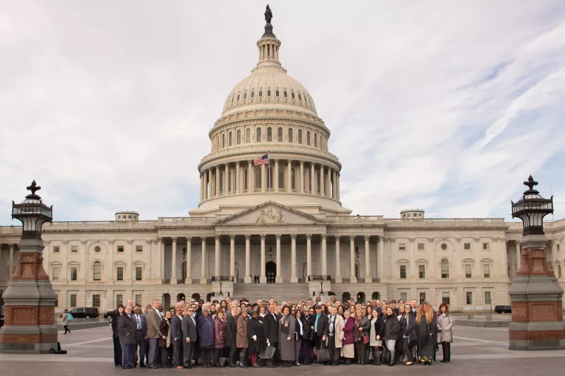 Group of people stand outside the Capitol building on a cloudy day