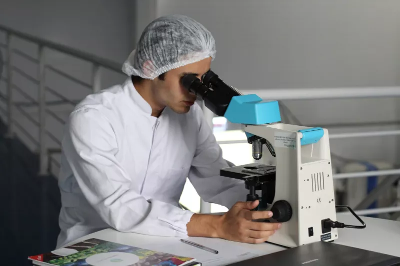 A male in a lab coat looking through a microscope