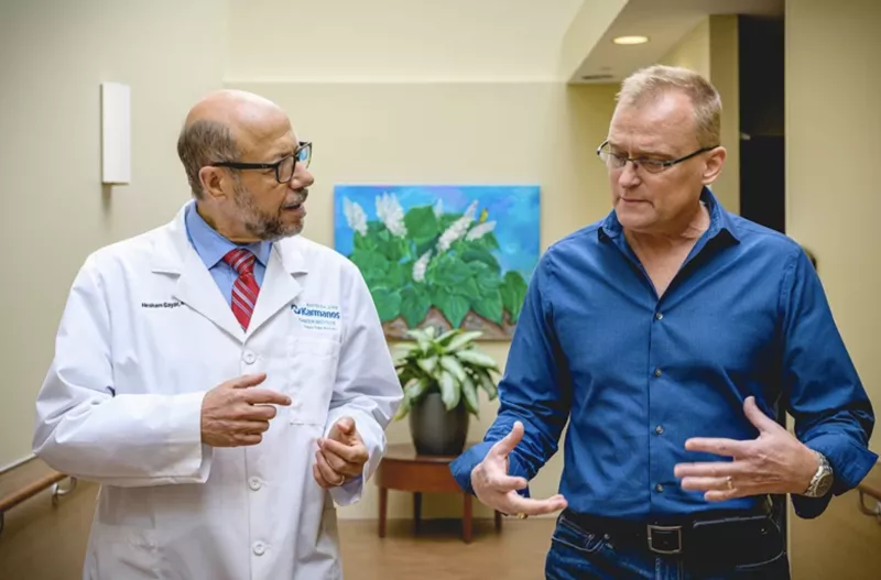 A doctor and a blond male patient in a blue shirt talking