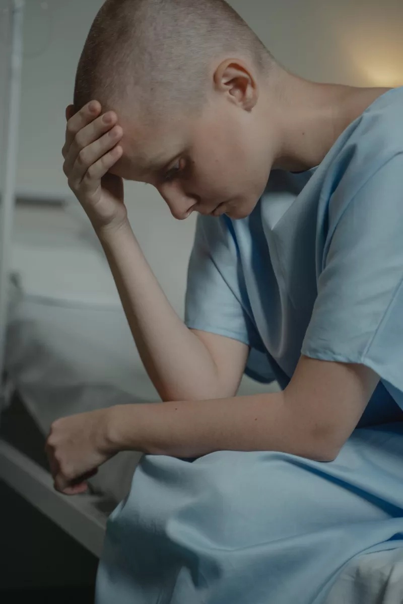 Man with a bold head wearing a hospital gown looking desolate