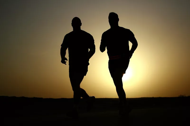 Dark silhouettes of two men running at sunset