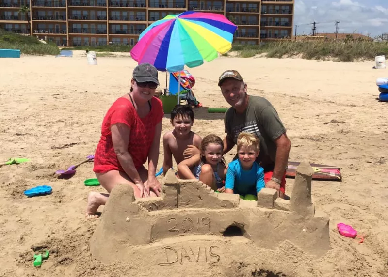 Barry Davis on family vacation the beach building sandcastle under a rainbow umbrella