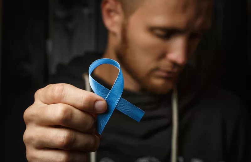 Man holding blue ribbon in forefront of image