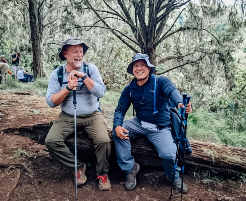 two men sitting and smiling on a hike