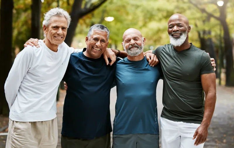 Four men standing with arms around each other shoulder to shoulder smiling
