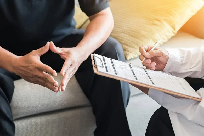 Image of hands of a patient and doctor. The doctor is holding a clipboard and appears to be consulting with the patient.