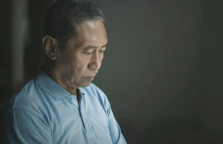 An asian man in a dark room looking down at the ground