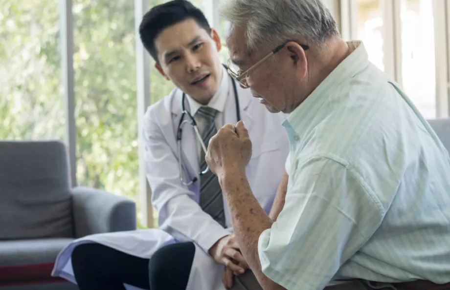 A young asian doctor speaking with an older male on a couch