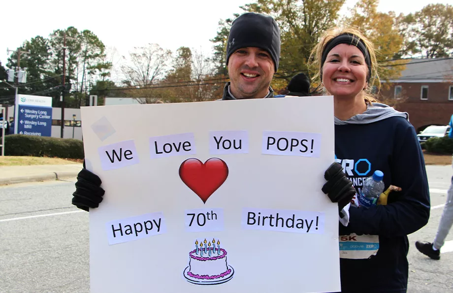 Two people holding a sign that says "We love you pop! Happy 70th birthday!"