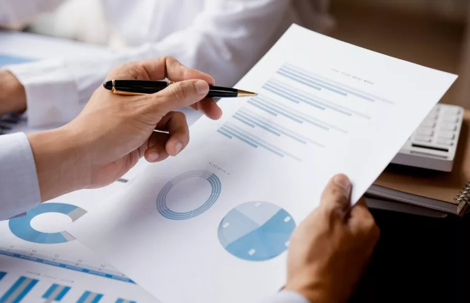 Image showing hands of a man who's holding a pen and looking over reports with charts