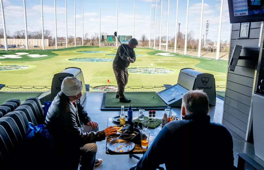 A man taking a golf swing at the top golf course with his friends