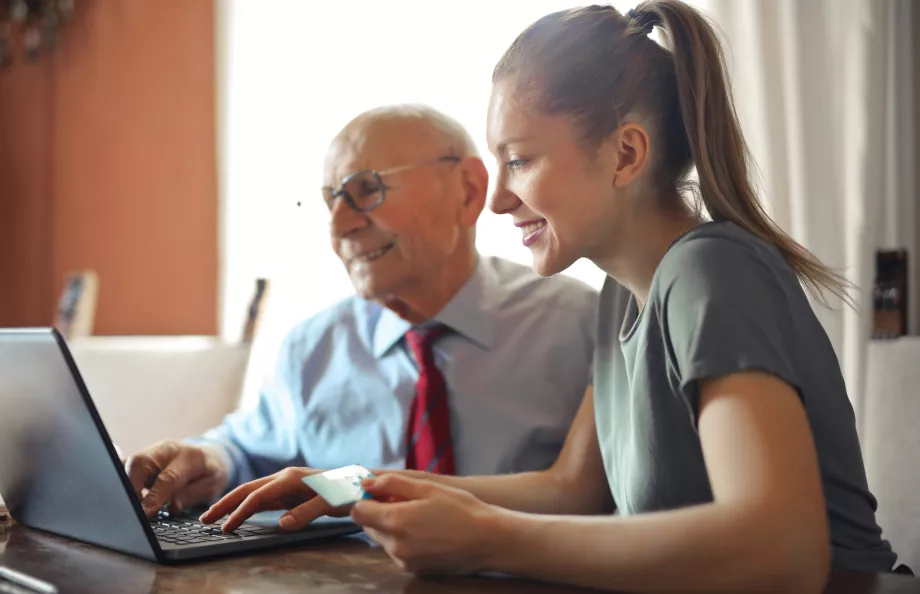 A younger woman helping an elderly man by using a laptop