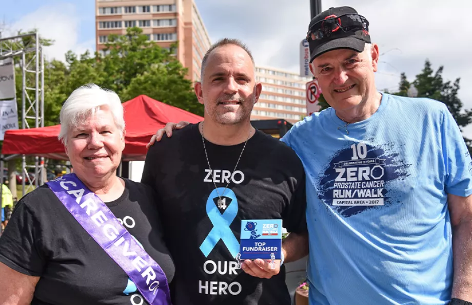 Top fundraiser holding award with a caregiver and another man