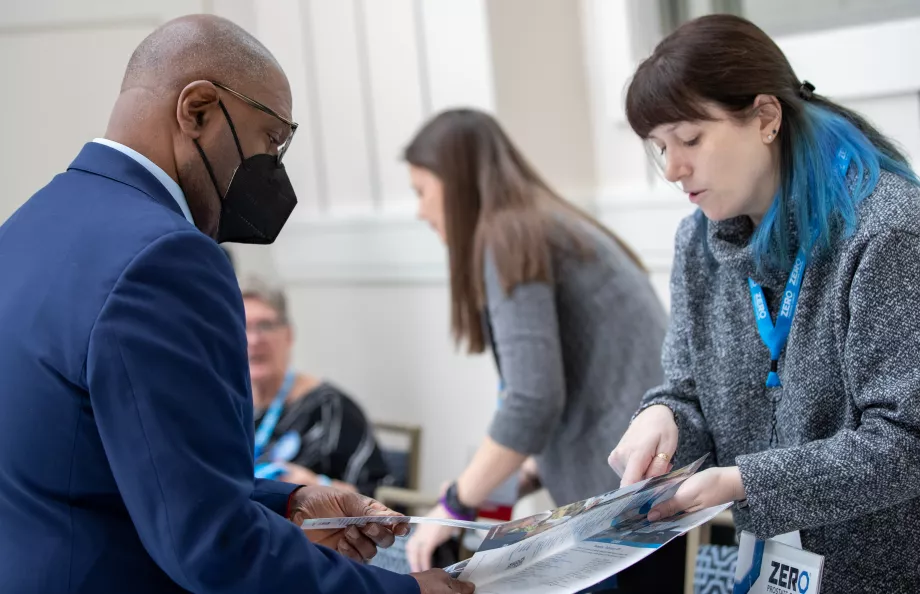A woman with blue hair highlights sharing reading materials with an African American man in a suit