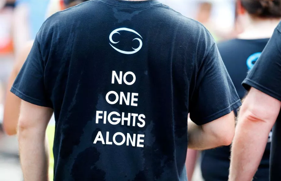 Man wearing a sweaty black t-shirt that says 'No one fights alone'
