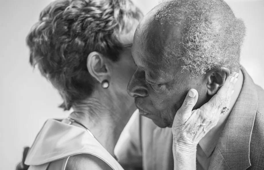 A black and white photo of a senior couple having an intimate moment as she kisses his cheek