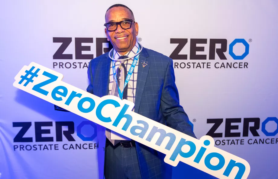 African American man in a suit holding a ZERO Champion sign