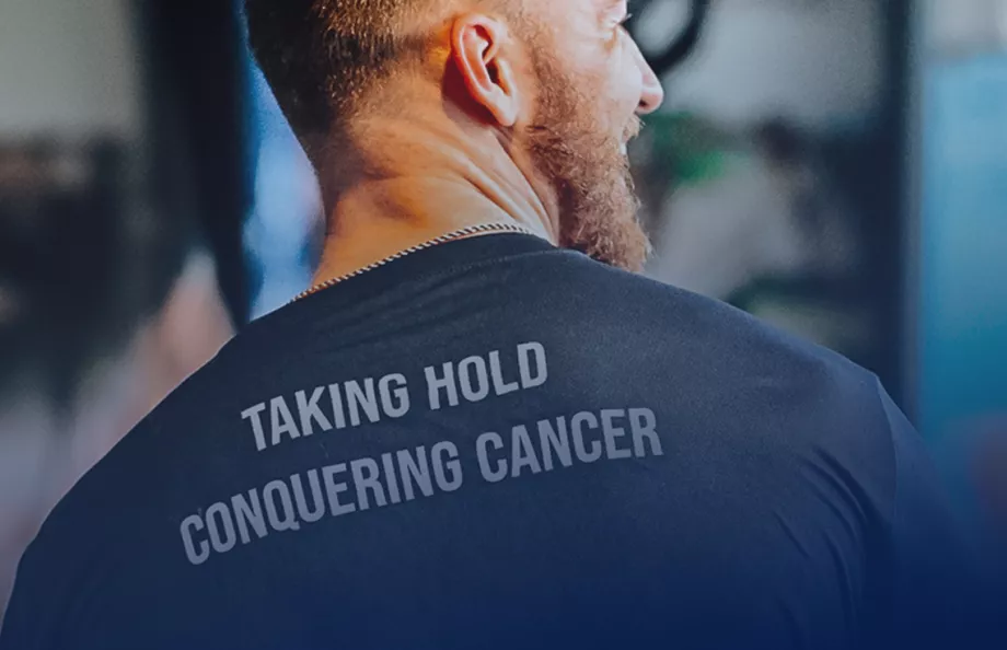 A man with his back towards the camera and his head turned to the right. His shirt says "Taking Hold Conquering Cancer".