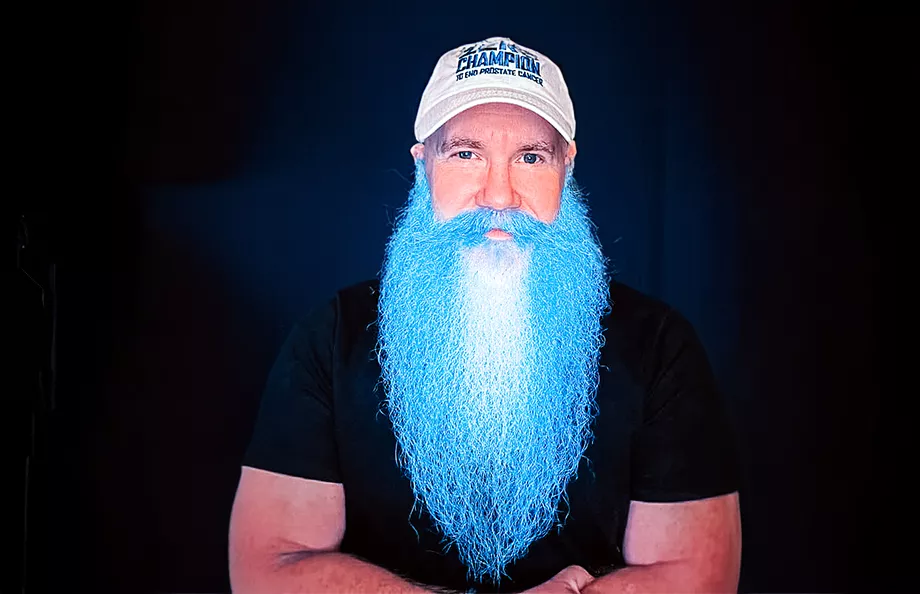 A white man with a long beard dyed blue wearing a ZERO Champions hat