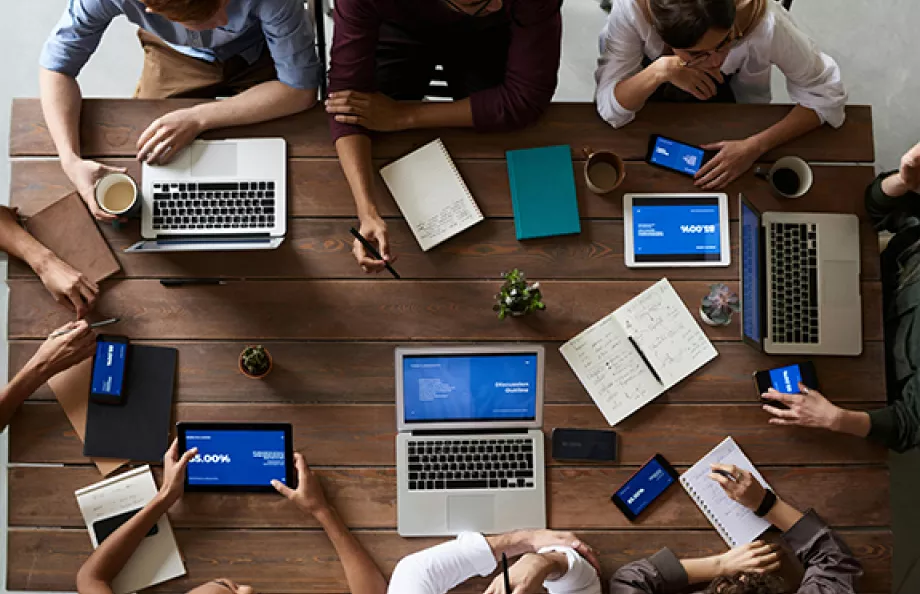 Group of people at wood desk with computers and coffee