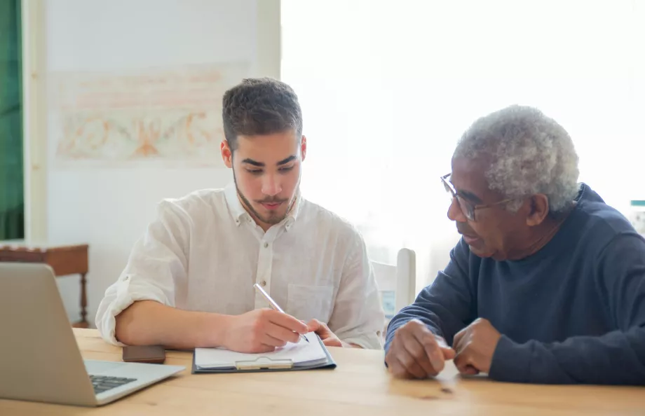 Stock photo of man helping an older man with a notebook and pen sitting at desk