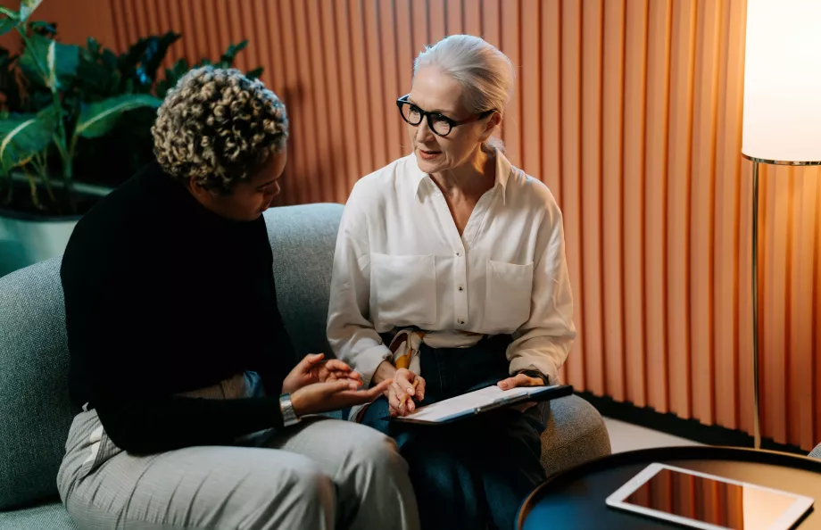 two women sitting on the couch, one showing the other a clipboard with math