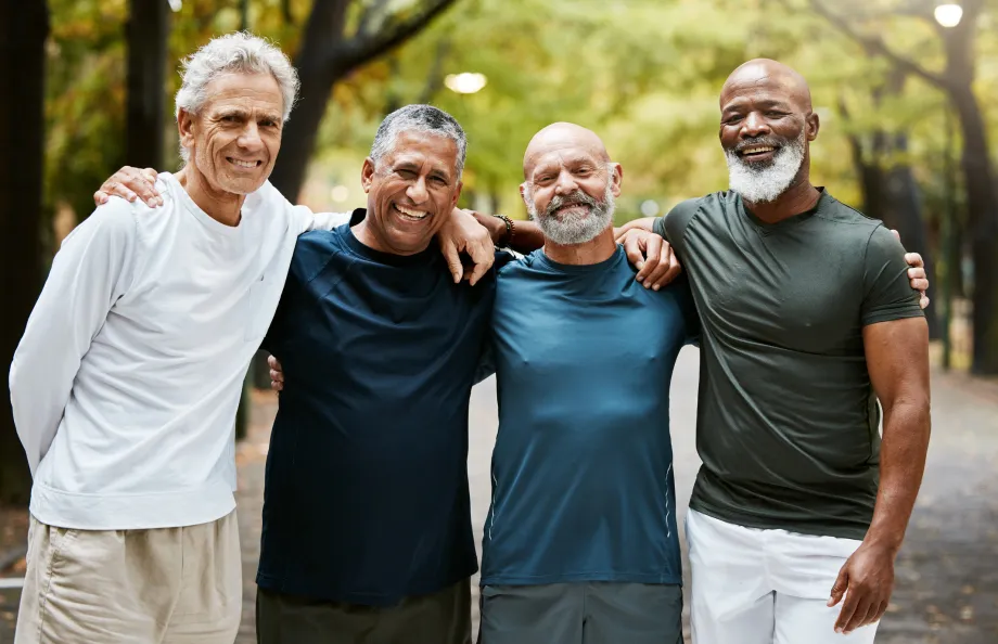 Four men standing with arms around each other shoulder to shoulder smiling